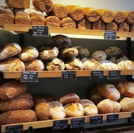 Houten schappen vol vers brood, met krijtbordjes met naam en prijs eronder